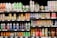 A grocery store shelf filled with a wide variety of colorful beverages in cans and bottles. The products include coconut water, carbonated soft drinks, teas, and fruit-flavored drinks. The packaging features vibrant colors and different languages.