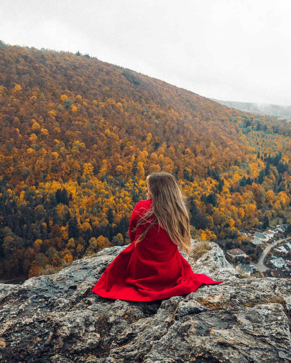Donna in felpa con cappuccio rossa seduta sulla roccia che guarda le montagne durante il giorno