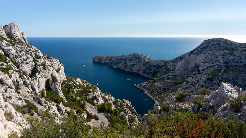 montagne verte et brune à côté de la mer bleue sous le ciel bleu pendant la journée