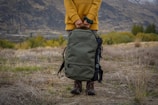 person in yellow jacket and black backpack walking on brown grass field during daytime