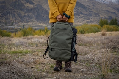person in yellow jacket and black backpack walking on brown grass field during daytime