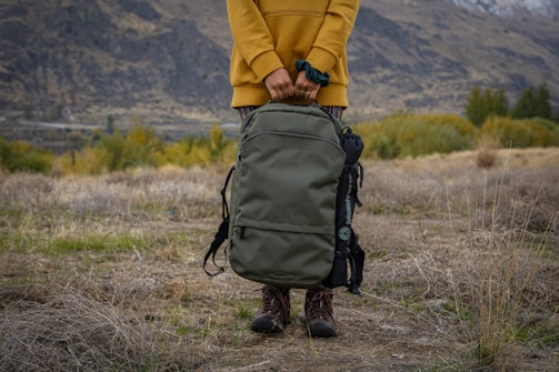 person in yellow jacket and black backpack walking on brown grass field during daytime
