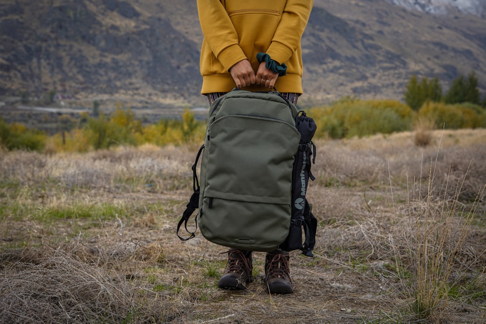 person in yellow jacket and black backpack walking on brown grass field during daytime