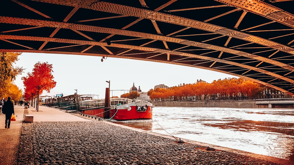 barco vermelho e branco na água sob a ponte durante o dia