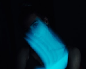 A moody, grain-textured frame capturing a shadowed figure in deep indigo light.