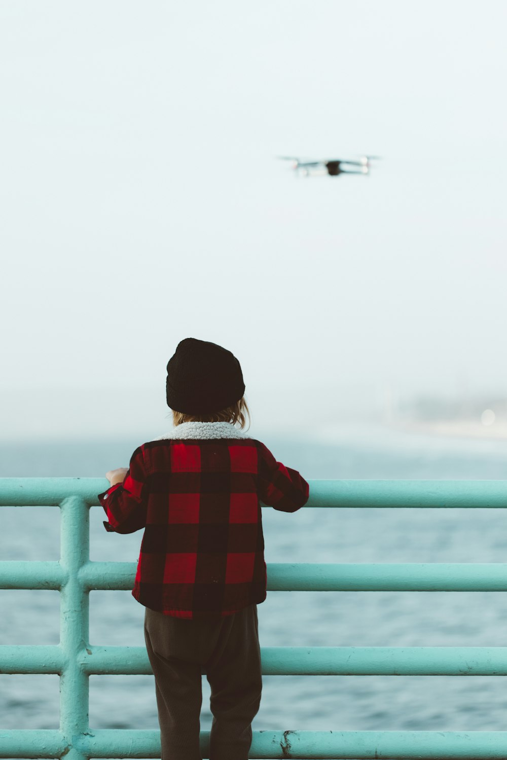 Enfant en chemise à carreaux rouge et blanc debout sur des balustrades en métal bleu pendant la journée