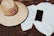 A straw hat with a red circular logo reading 'Quiksilver Bali Surf Academy' is placed on a wicker surface next to a white towel. Beside the towel, there is a smartphone with a black screen.