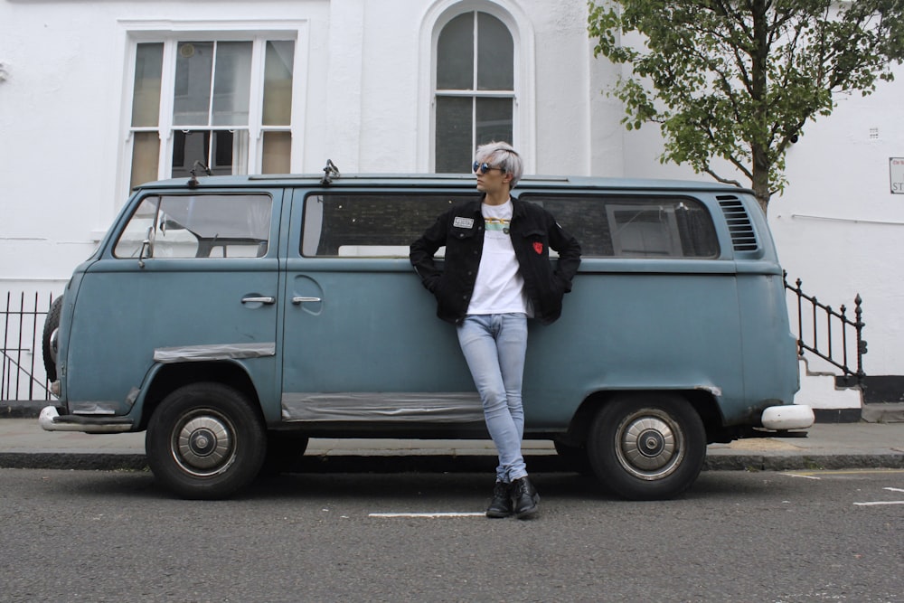 man in black jacket and white pants sitting on blue van