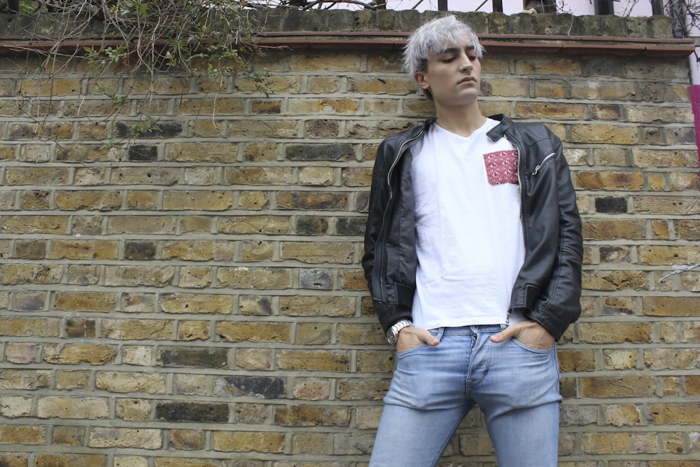 man in black zip up jacket standing beside brick wall