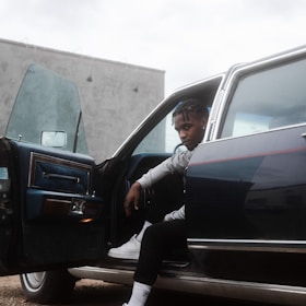 A professional driver opening the car door for a passenger in a city setting.