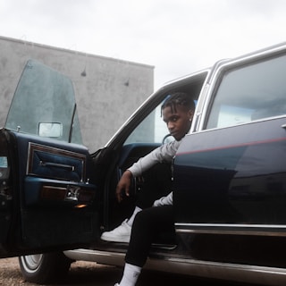 A professional driver opening the car door for a passenger in a city setting.