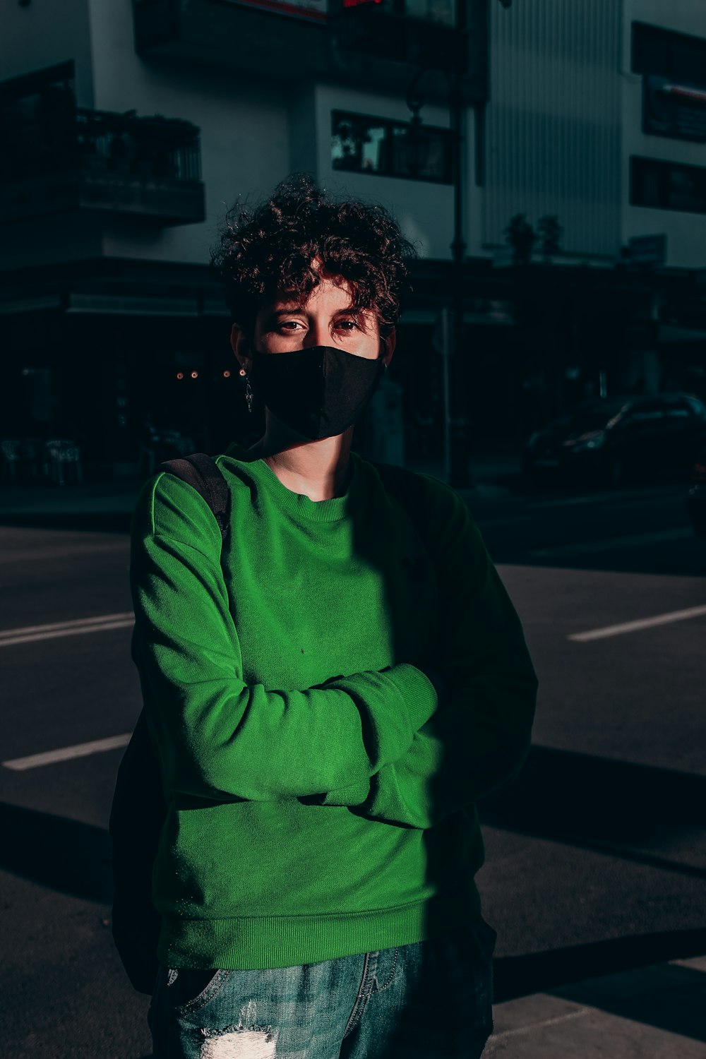 Mann in grünem Pullover mit schwarzer Maske steht nachts auf dem Bürgersteig