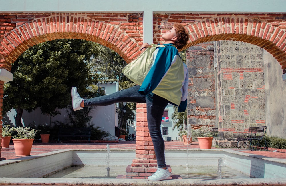 woman in blue and white jacket and blue denim jeans standing on brown concrete brick