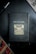 A notebook with a black cover featuring a gold illustration of a typewriter and the words 'think, write, create' on the front. It is placed on a dark surface accompanied by a black pen and a partial view of a newspaper or magazine.