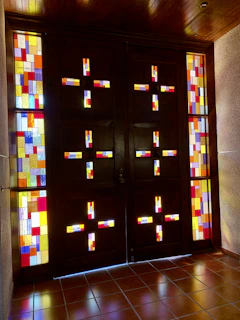 A modern wooden door with colorful stained glass panels glowing in natural sunlight