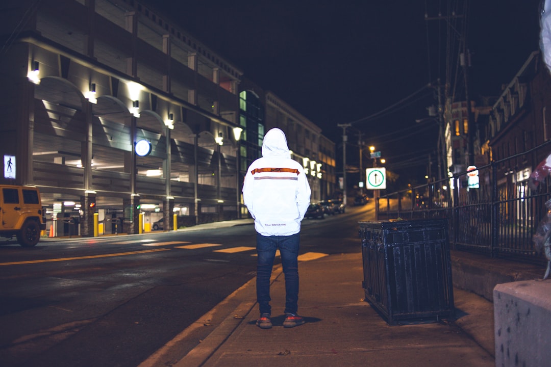 man in white hoodie standing on sidewalk during night time