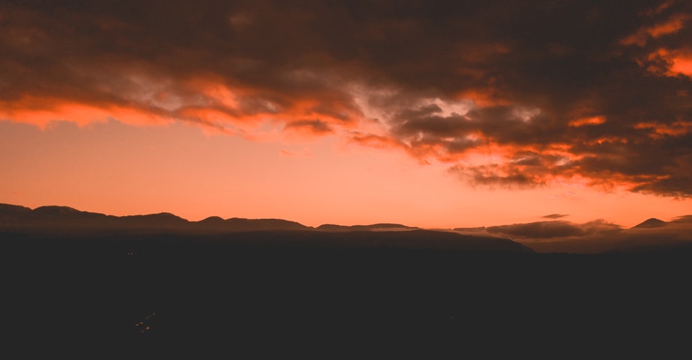 Silhouette des Berges unter orangefarbenen und grauen Wolken