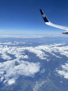An aerial shot of a snowy mountain range with a plane flying above the peaks.