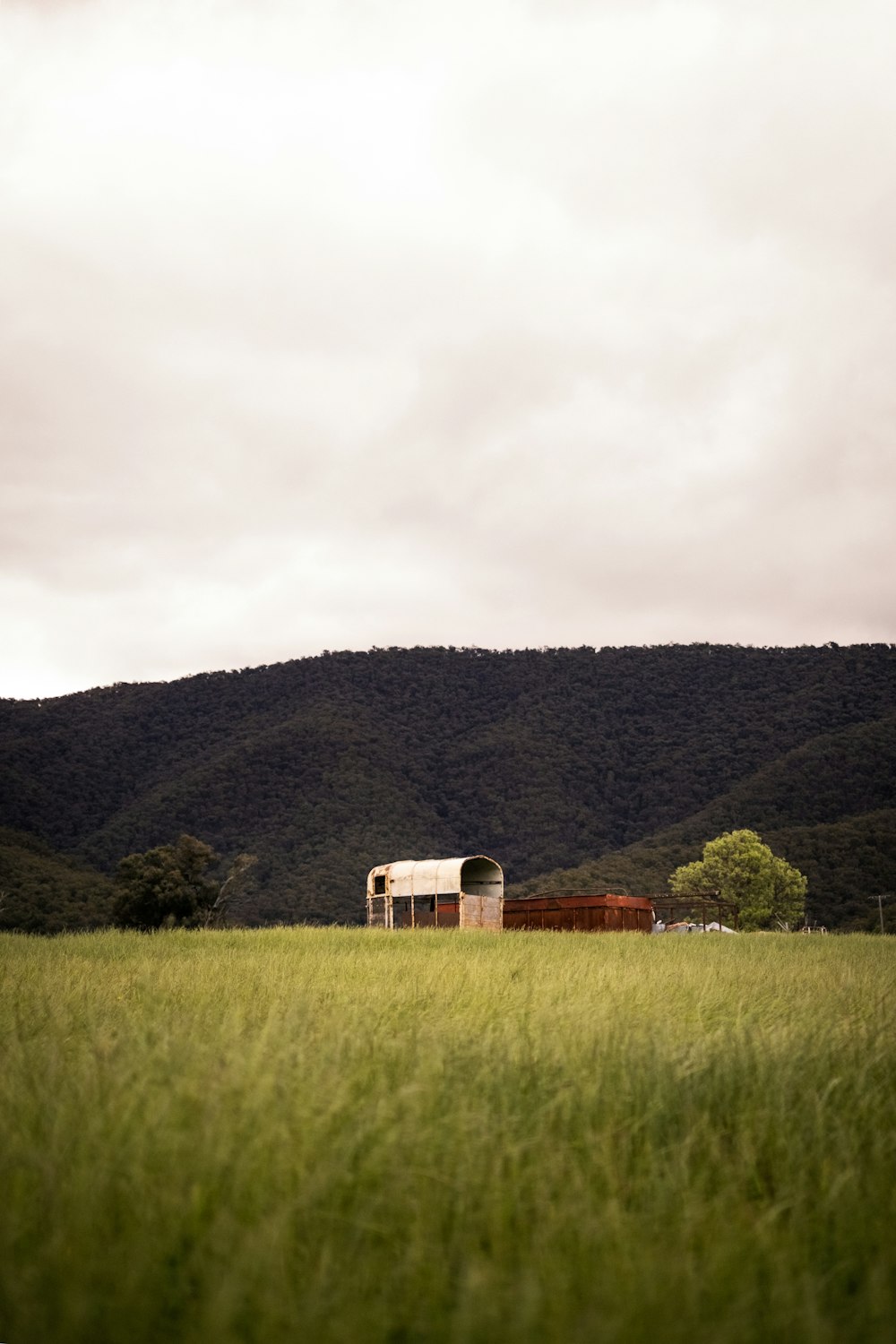 Maison en bois brun sur un champ d’herbe verte près de montagnes vertes sous un ciel nuageux blanc pendant la journée