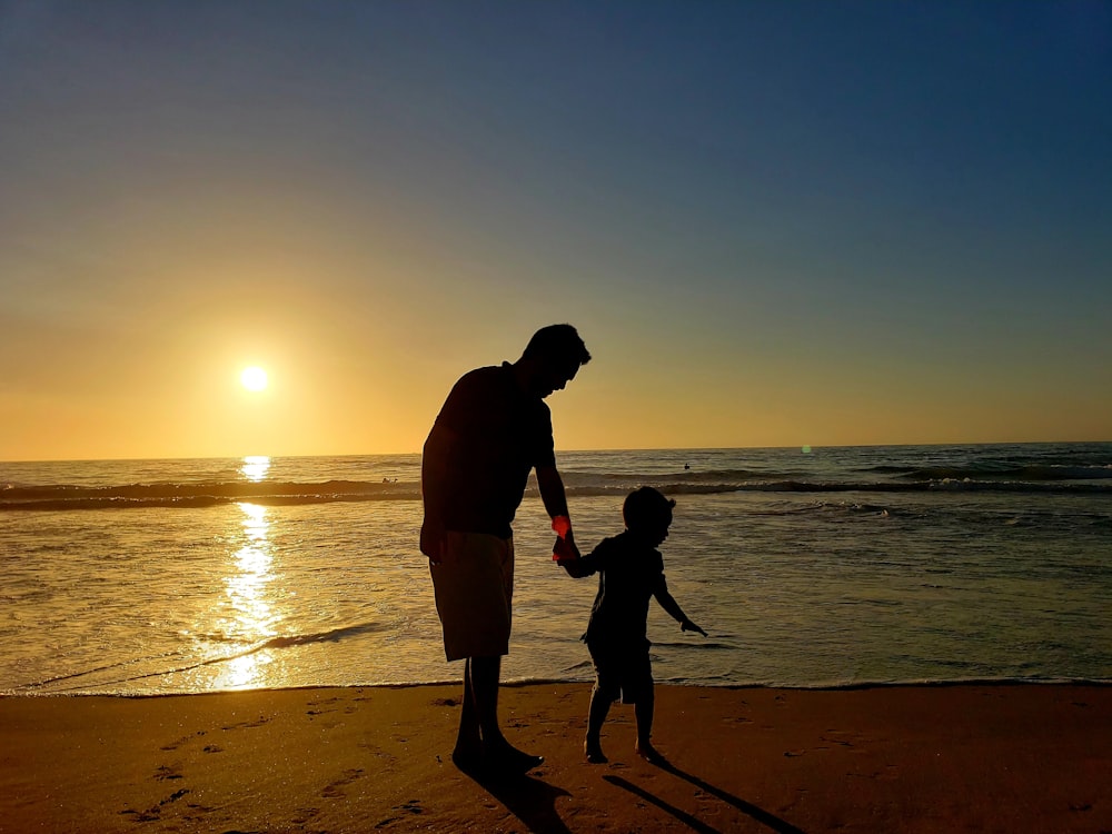 Silhouette von Mann und Frau, die bei Sonnenuntergang am Strand Händchen halten