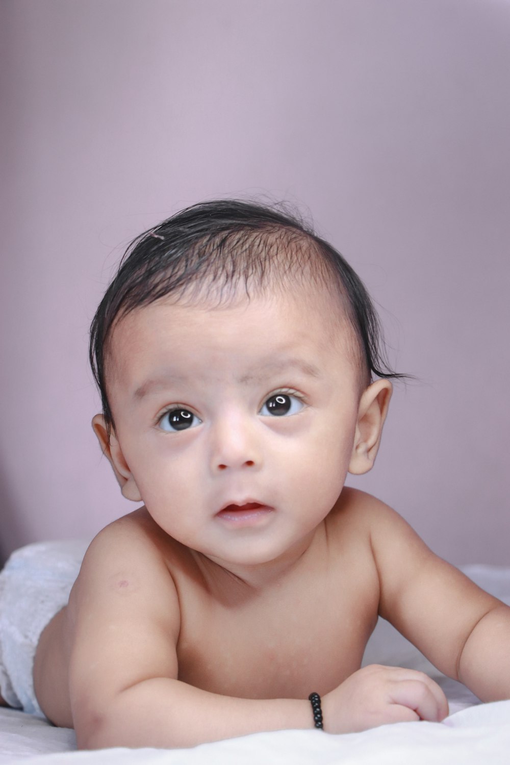 topless baby lying on white textile