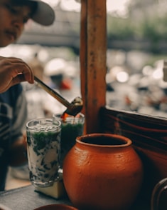 person holding brown ceramic pot pouring water on clear drinking glass