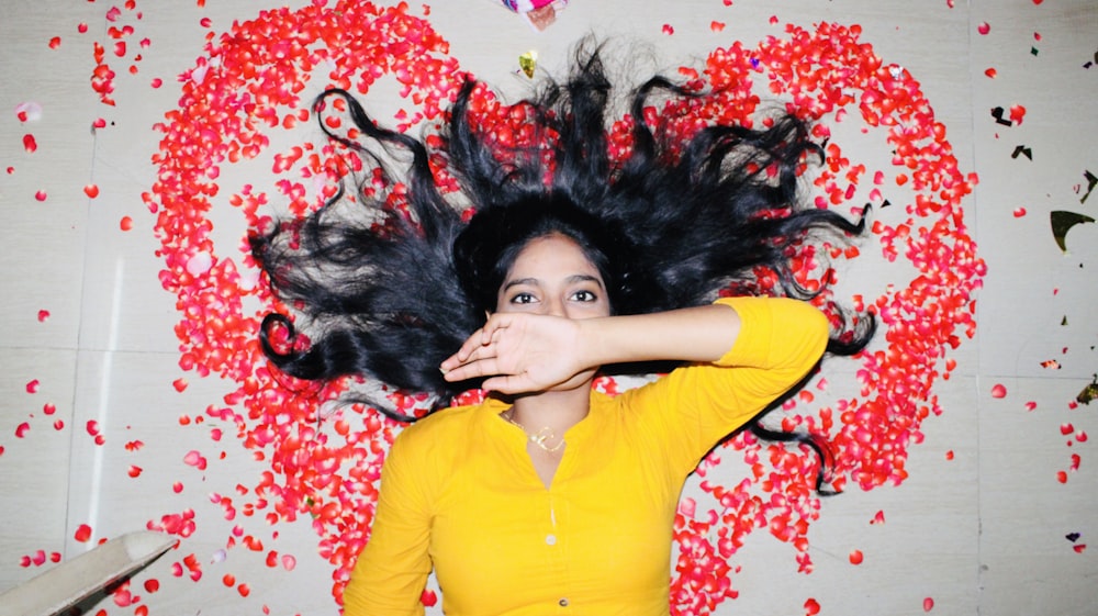 woman in yellow long sleeve shirt lying on red and white floral textile