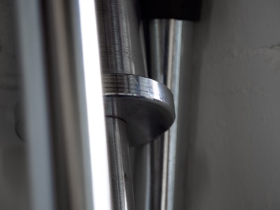 Close-up view of metallic cylindrical rods with smooth surfaces, reflecting light in a low-light setting. The rods are arranged vertically and parallel to each other, with a portion of one rod prominently visible in the center.