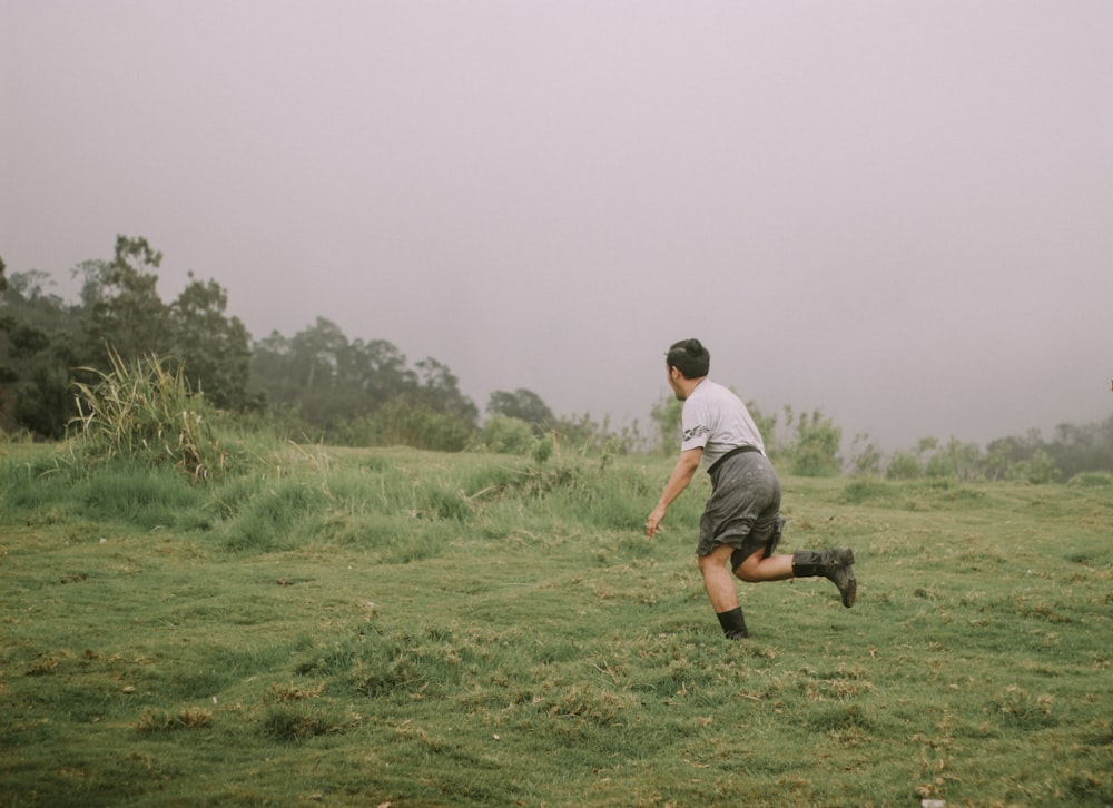회색 티셔츠와 검은 반바지를 입은 남자가 낮에 푸른 잔디밭을 달리고 있다