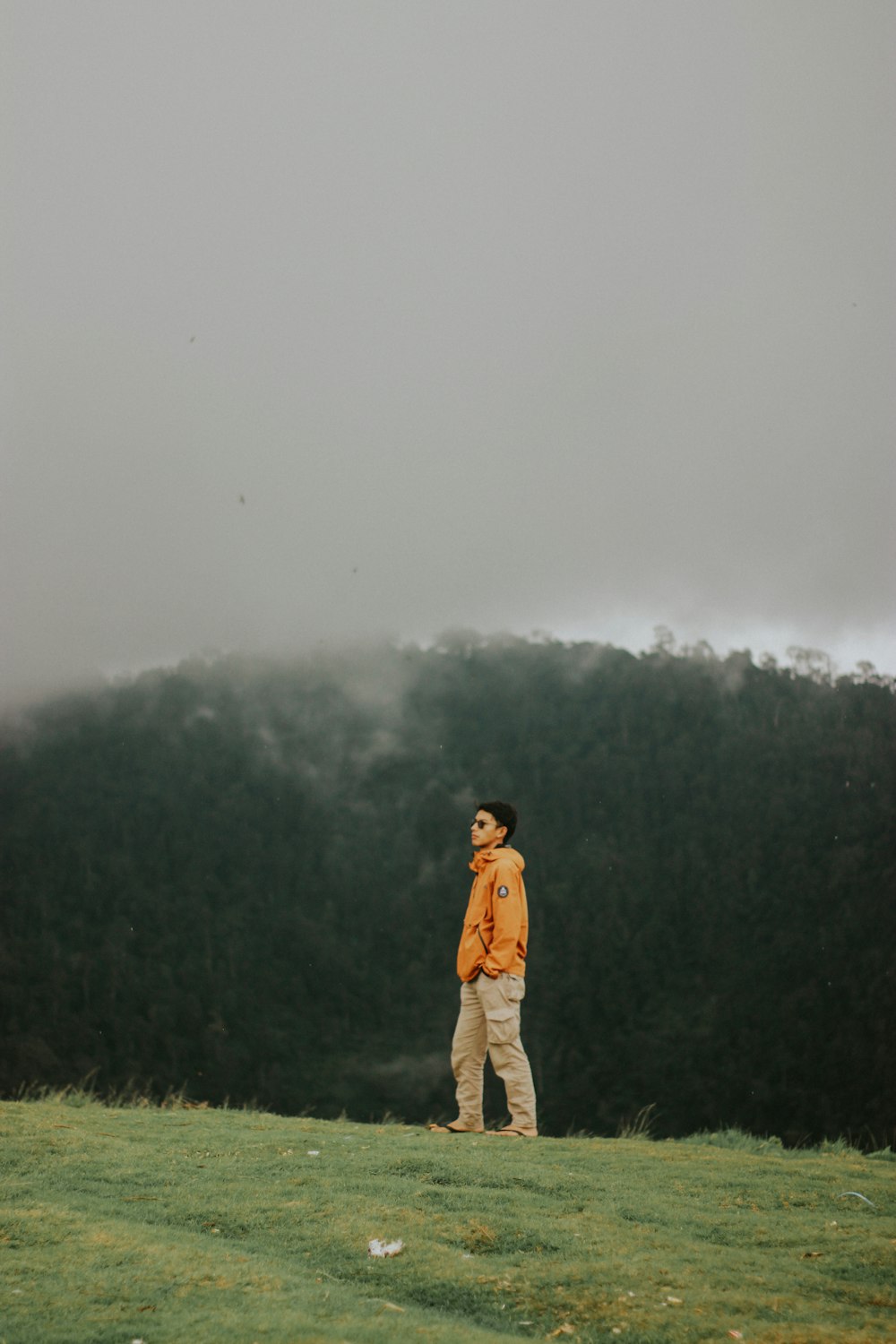 man in brown jacket standing on green grass field during foggy weather