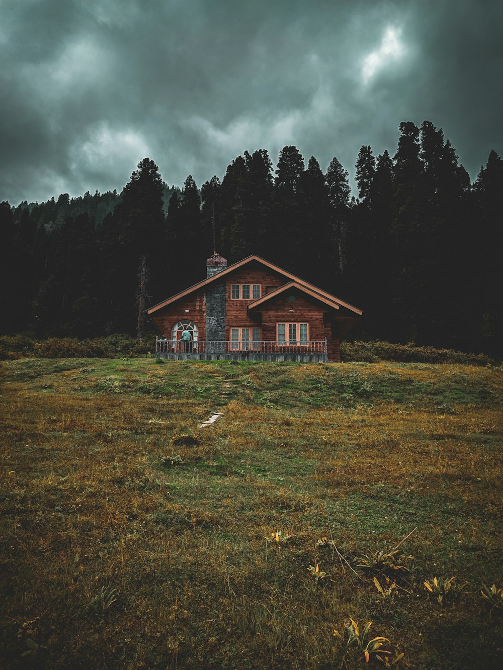 brown wooden house on green grass field near green trees under gray clouds