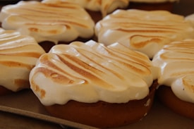 Golden-brown baked goods topped with smooth, lightly toasted meringue on a baking tray.