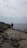 A peaceful hiker walking along a rocky coastal path near Scivu beach under a cloudy sky.
