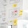 A whiteboard or wall is filled with paper sheets and sticky notes containing diagrams, sketches, and notes. Prominent features include hand-drawn flowcharts with symbols and arrows, as well as several colored sticky notes with handwritten words like 'Feedback' and 'Infos + Features'. The central sheet displays a layout with text and colored dots, possibly representing an interface design or process.
