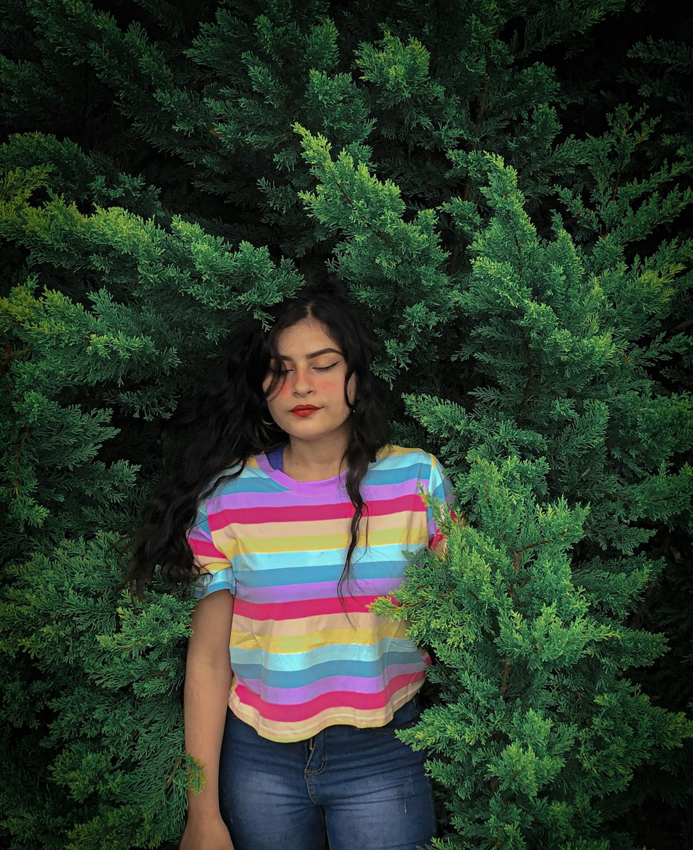 woman in pink white and blue stripe shirt standing near green plant