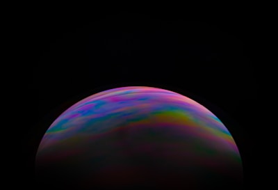 A dark background highlights a colorful, spherical object with swirling patterns of pink, blue, green, and yellow hues. The object resembles a bubble or planet, occupying the lower half of the image.