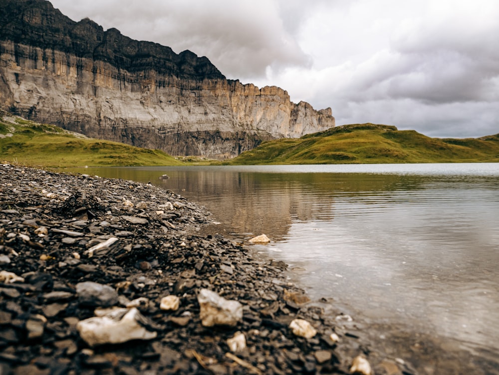 brown rocky mountain beside river under cloudy sky during daytime