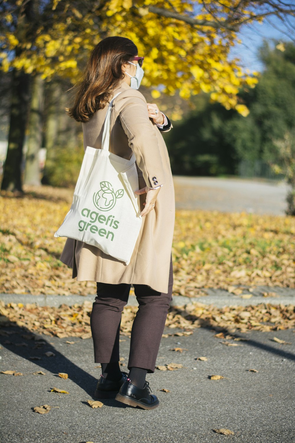 Mujer con abrigo beige y pantalones negros que llevan bolso blanco