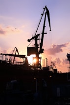 Heavy machinery trucks and cranes lined up under an industrial sunset.