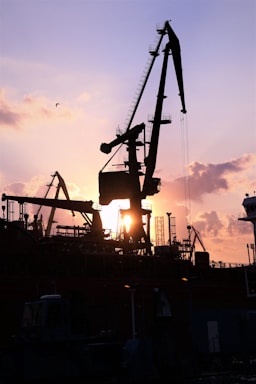 Heavy machinery trucks and cranes lined up under an industrial sunset.