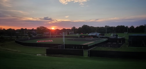A coach and a young baseball player shaking hands on the field at sunset.
