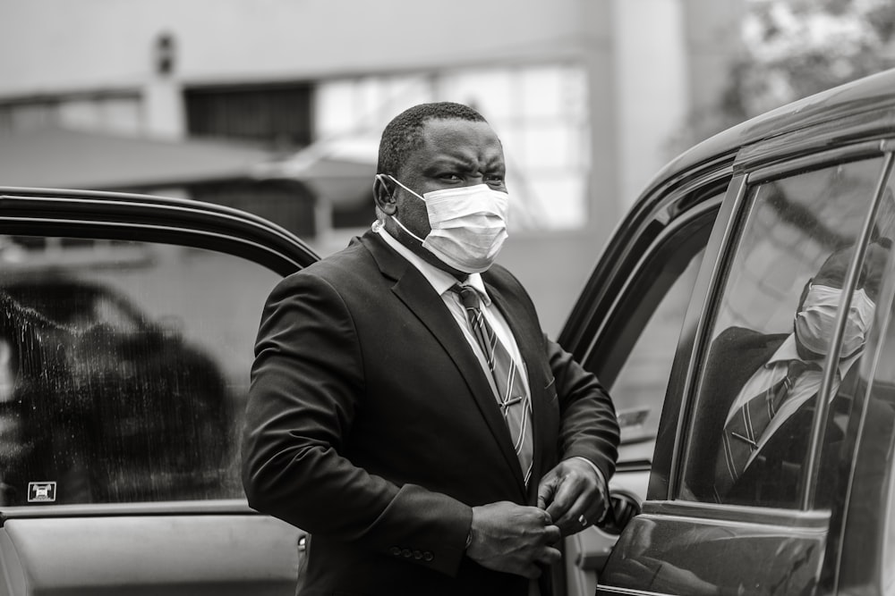 man in black suit jacket smoking cigarette in grayscale photography