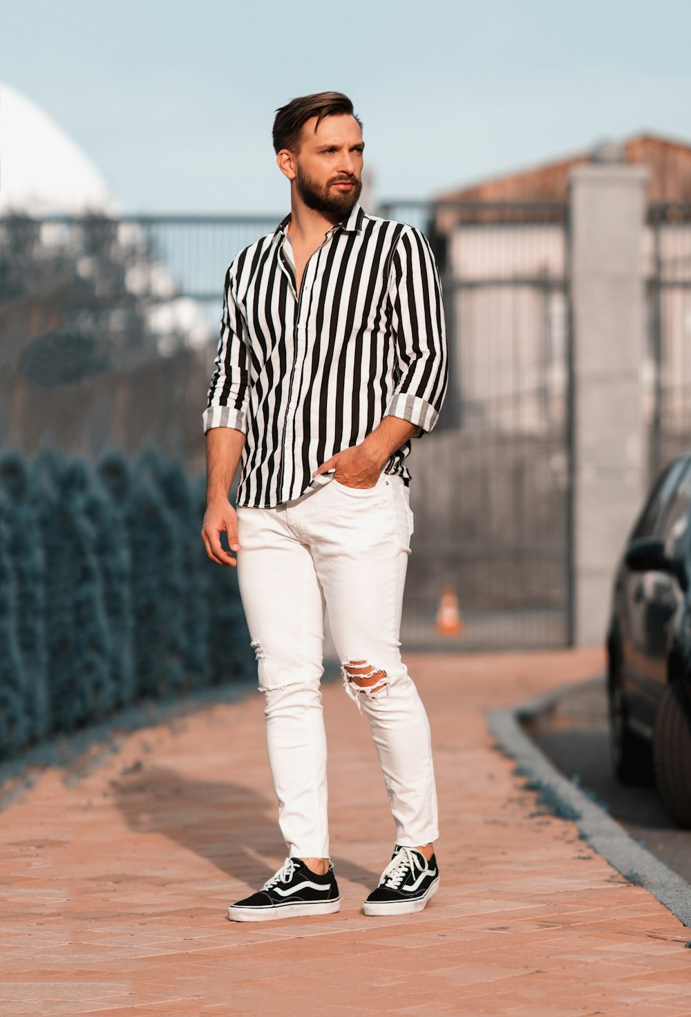 man in black and white stripe button up shirt and white pants standing on brown concrete