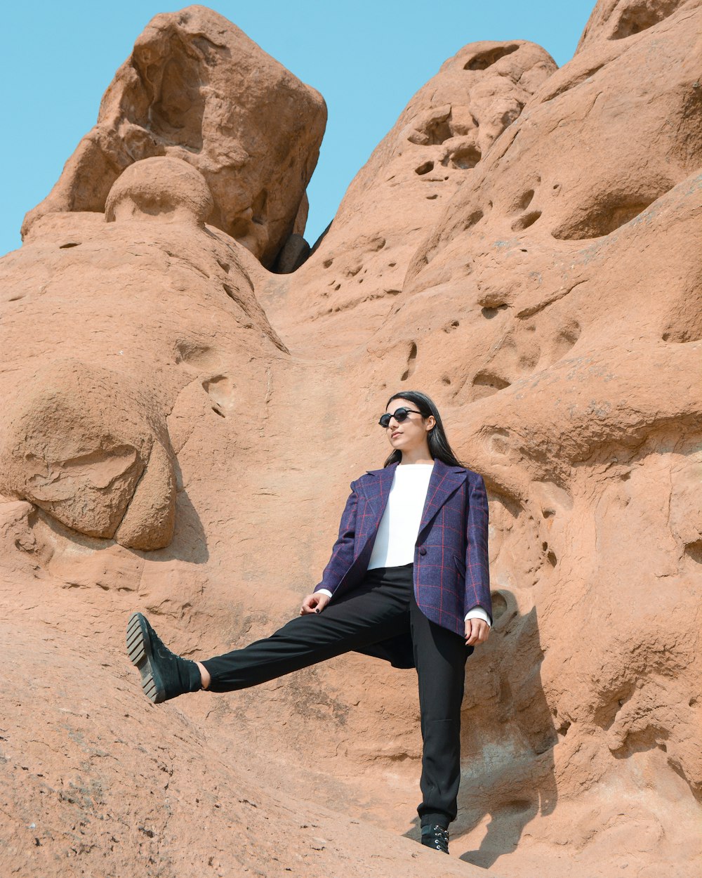 woman in black blazer and black pants sitting on brown rock formation during daytime