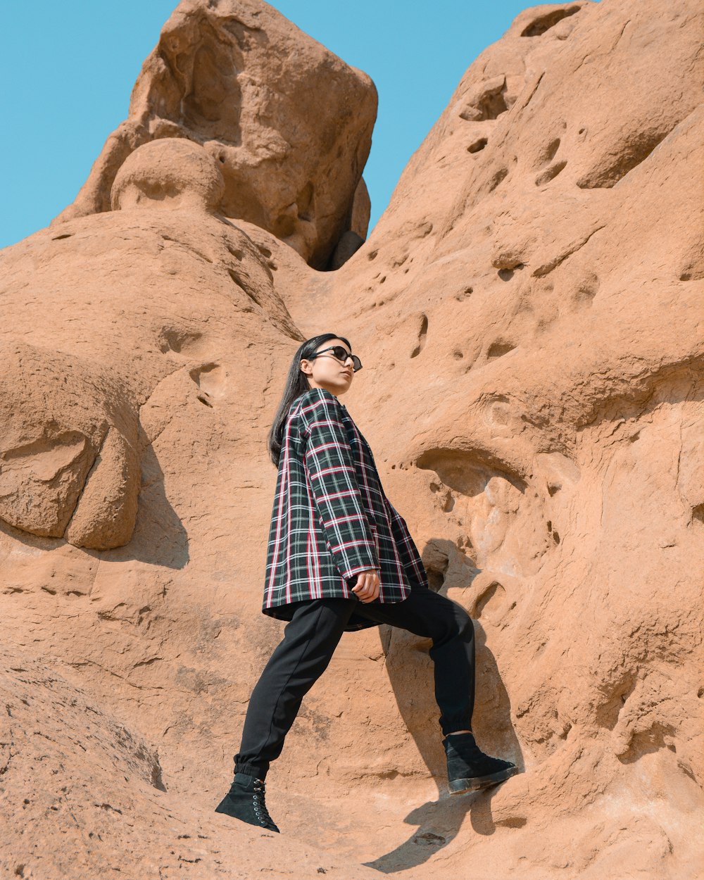 man in blue and white plaid dress shirt and black pants standing on brown rock formation