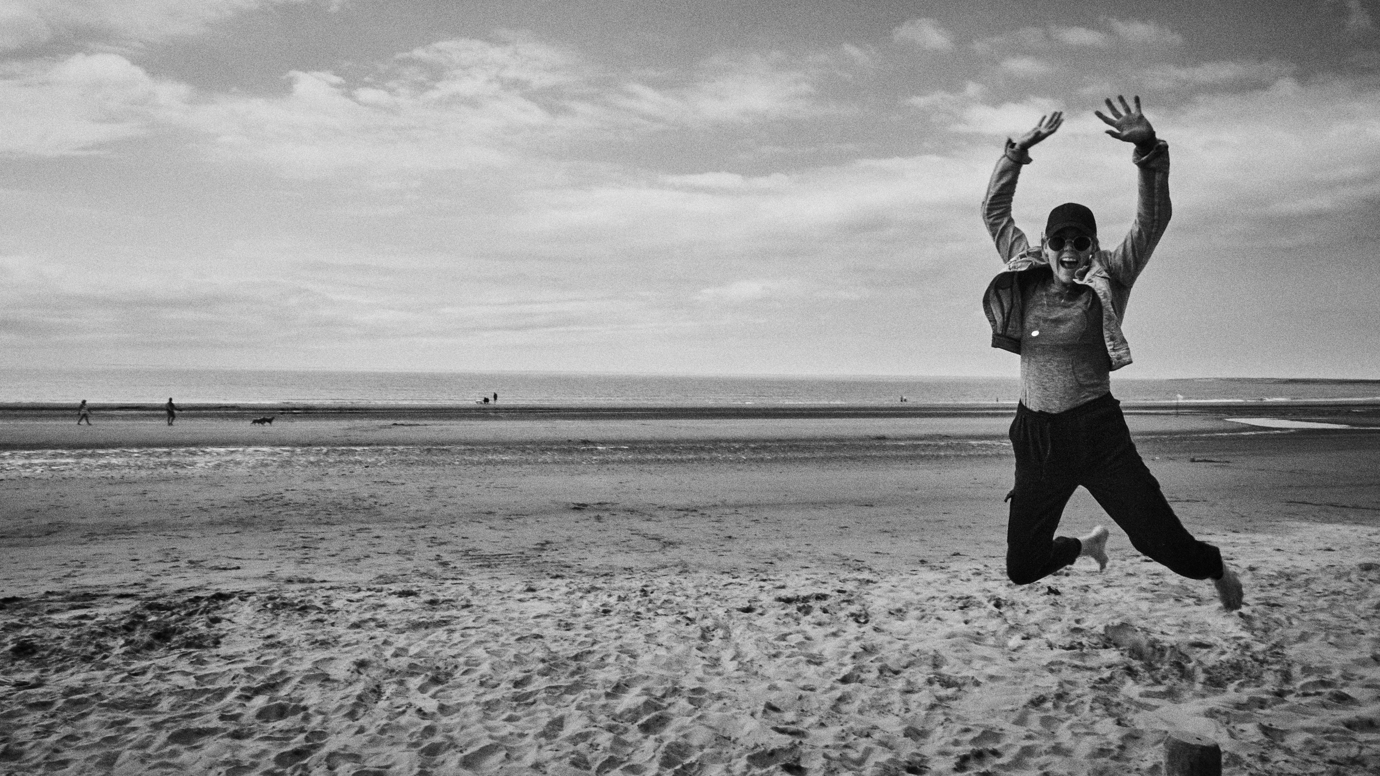 grayscale photo of man in black pants standing on beach