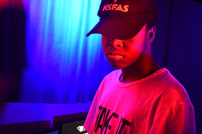 A stylish black cap with golden embroidered logo glowing softly under neon studio lights.