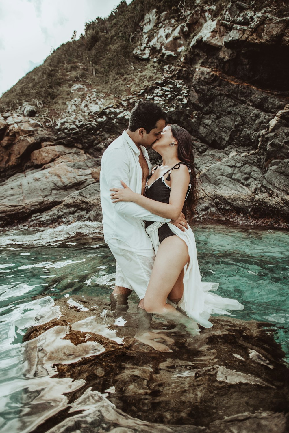 couple kissing on rocky shore during daytime