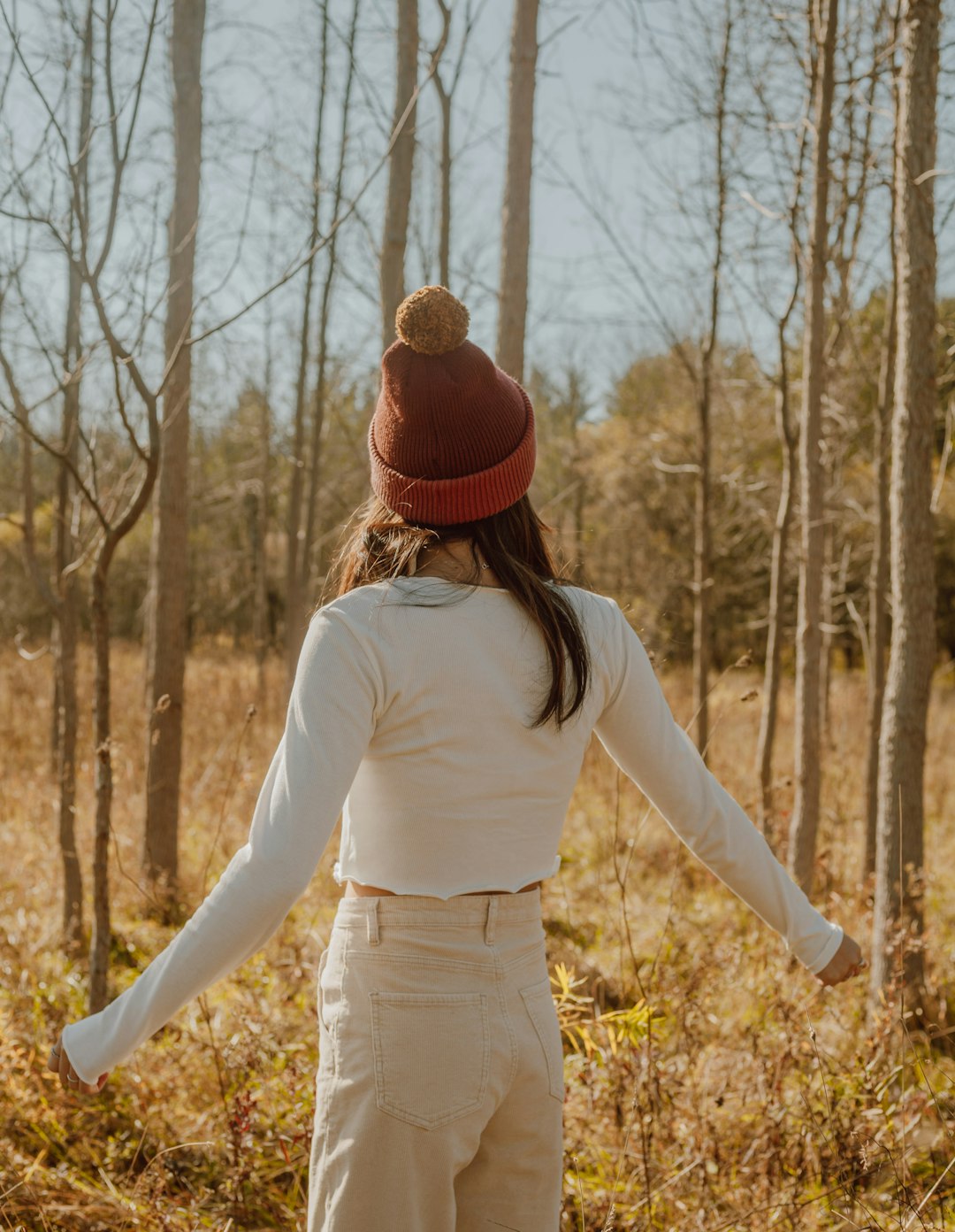 woman in white long sleeve shirt and red knit cap standing on brown grass field during