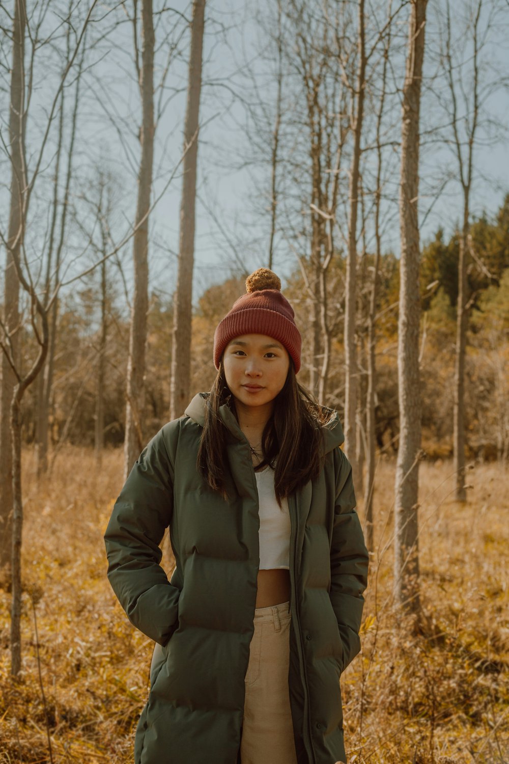 woman in green jacket and red knit cap standing near bare trees during daytime